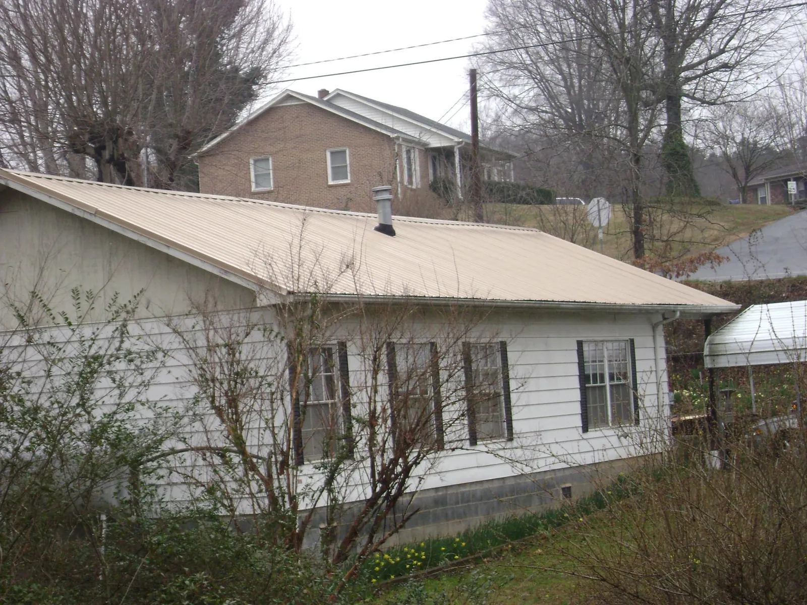 Tan metal roof on a white sided house set into a hillside — Commercial Roofing by Roofing Brothers in Omaha